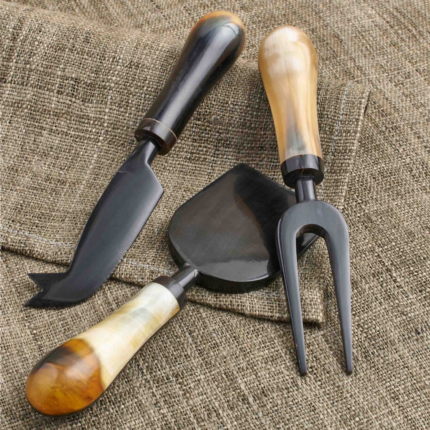 Set of three water buffalo horn cheese tools with wooden handles on a textured fabric background