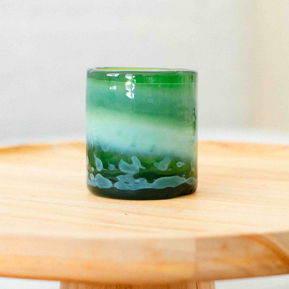 Green glass candle holder on a wooden surface with a white background