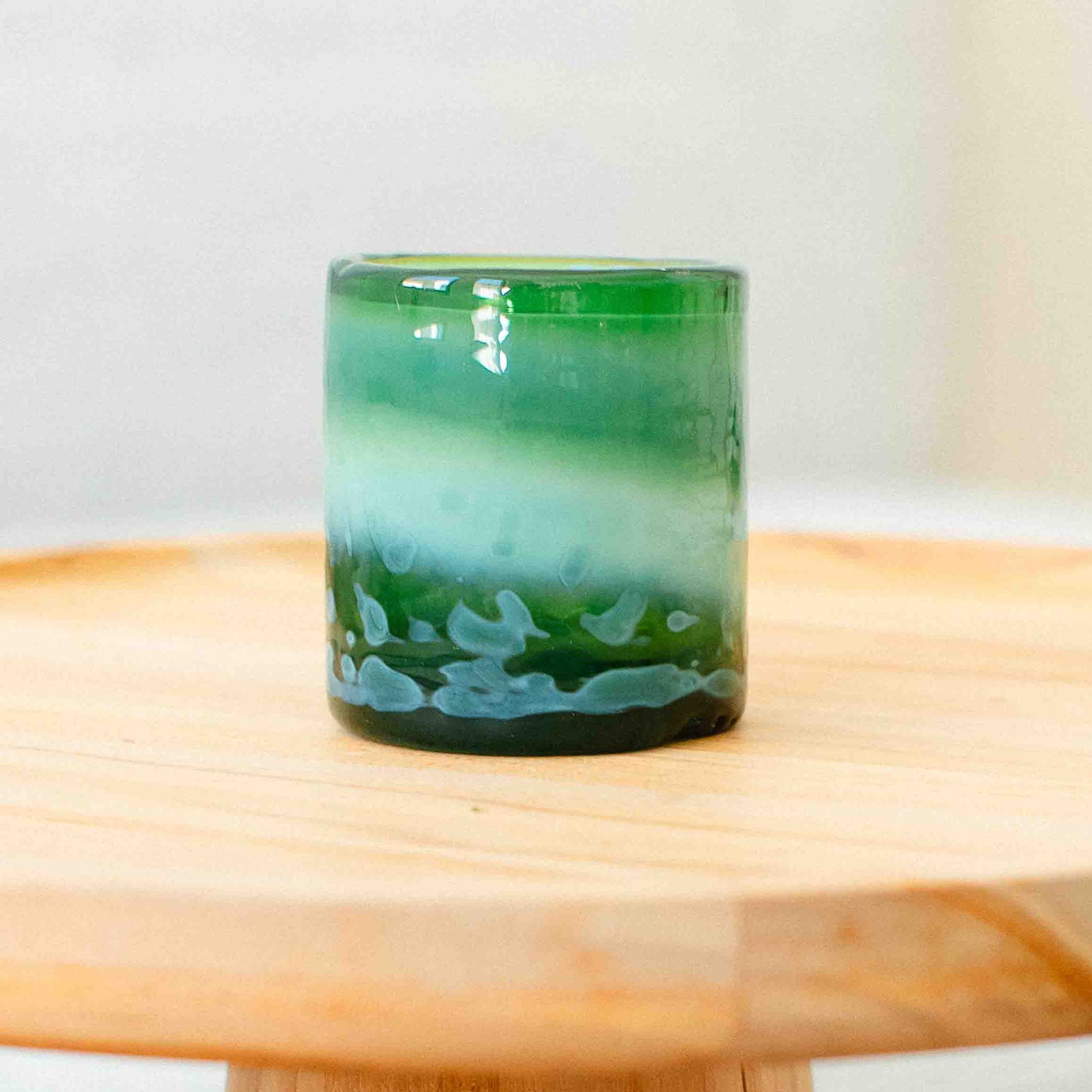 Green glass candle holder on a wooden surface with a white background