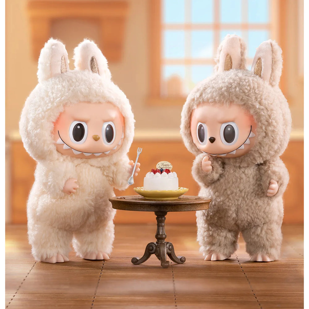 
                      
                        The MONSTERS Exciting Macaron series Labubus standing around a small table with a cake on it.
                      
                    