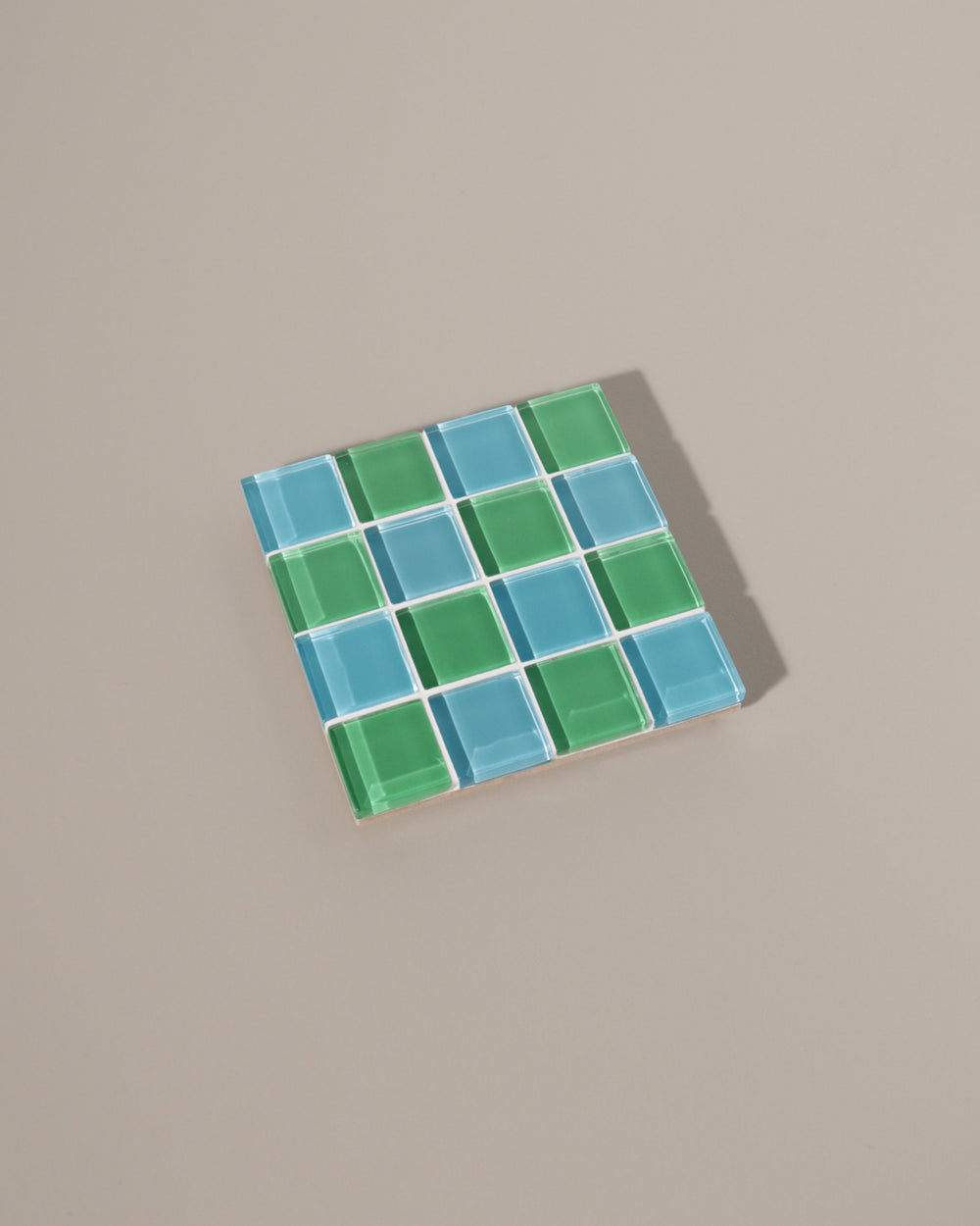 A handcrafted glass tile coaster with a green and blue checkered design.