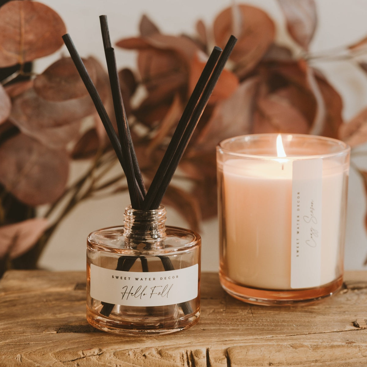 Amber glass reed diffuser with black sticks and lit cream soy candle in clear jar, cozy fall home decor set