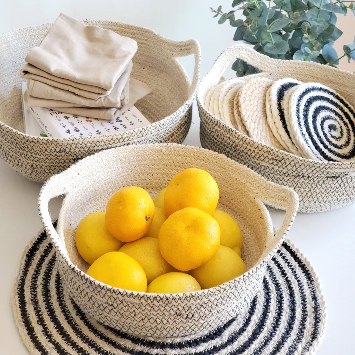 Woven baskets with lemons, folded cloths, and a plant on a light surface.