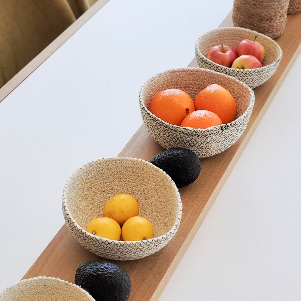 Three woven bowls containing fruits on a wooden tray with a white background