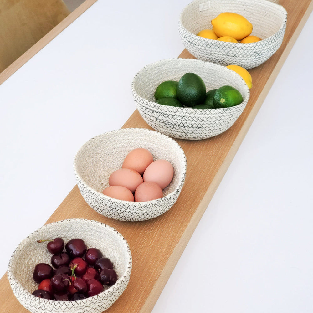 Set of woven bowls containing eggs, limes, and cherries on a wooden surface.