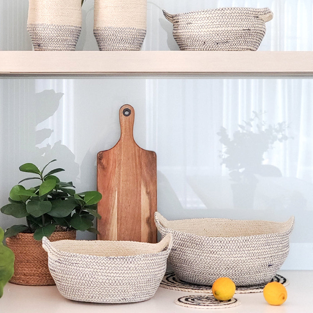 
                      
                        Woven baskets, a wooden cutting board, and potted plants on a shelf with a white background.
                      
                    