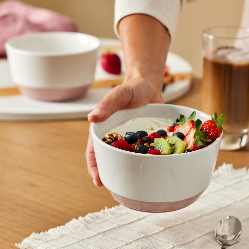 
                      
                        Person holding a bowl of fruit salad with yogurt on a wooden table.
                      
                    