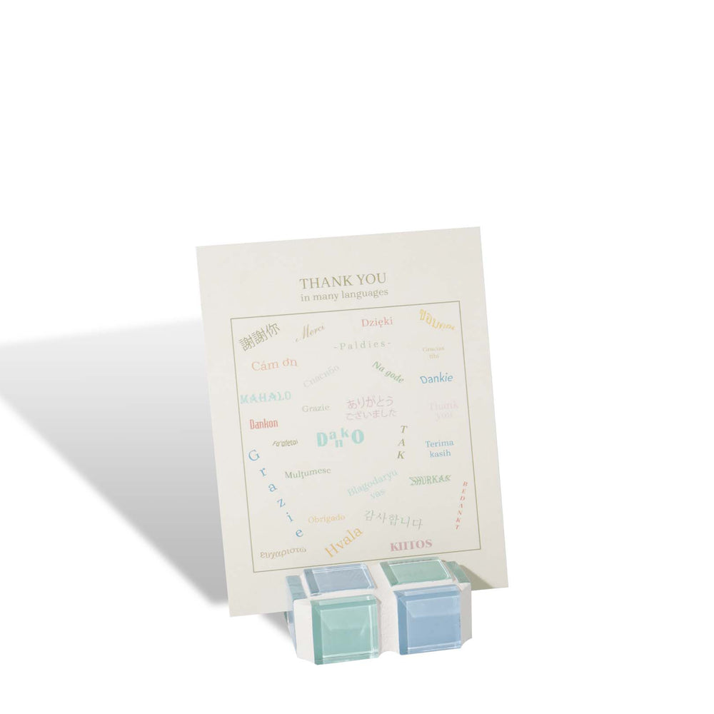 A small glass tile picture stand in blue and seafoam green hues in checkered pattern, propping up a picture or card inside.