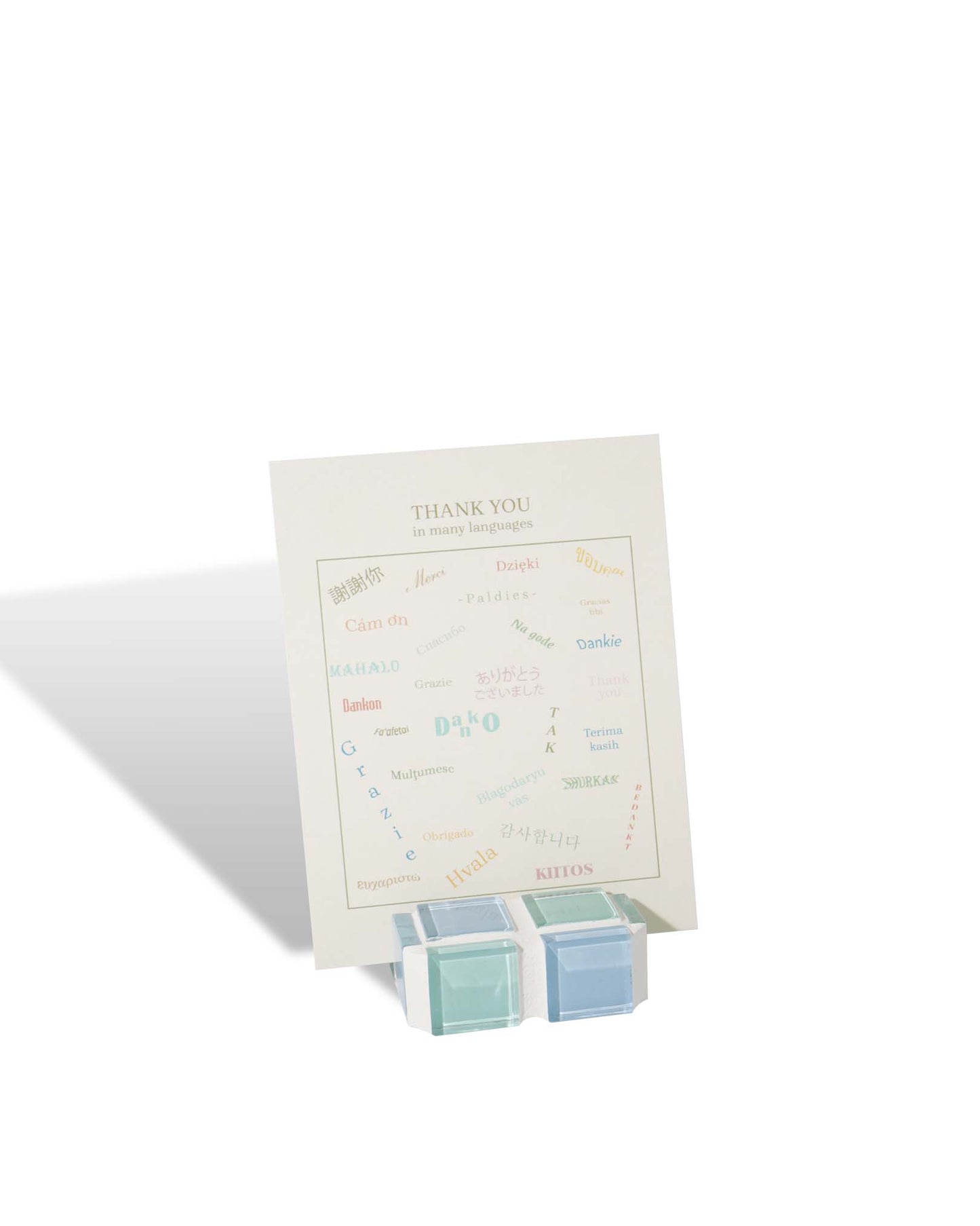 A small glass tile picture stand in blue and seafoam green hues in checkered pattern, propping up a picture or card inside.