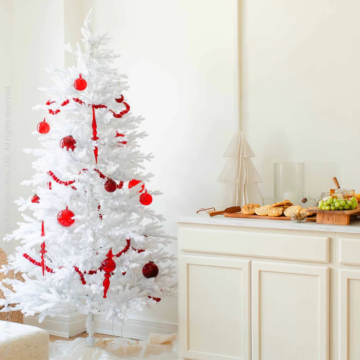 Moroah™ Mouth Blown Red Glass Ornaments on white tree next to holiday spread.