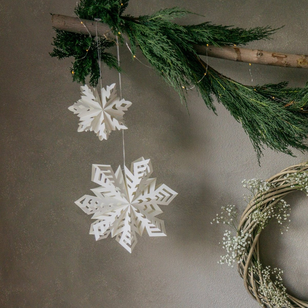 
                      
                        Two Flurry™ Hanging Paper Snowflakes hanging from a branch against a gray wall.
                      
                    