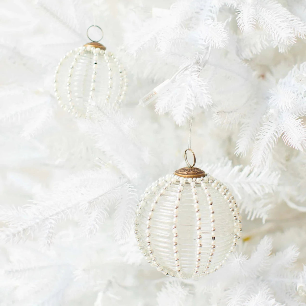 Two Kierling™ Mouth Blown Beaded Glass Ornaments hanging from white Christmas tree